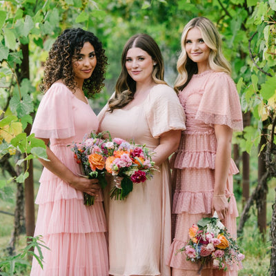 Three ladies standing in a vineyard wearing Modest Bridesmaid Dresses