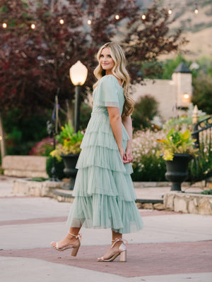 A lady walking down a pathway with a seafoam modest prom dress.