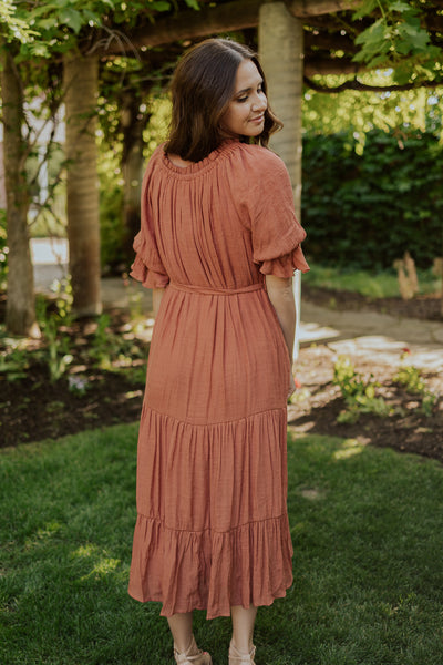 A back shot of our modest dress featuring tiered maxi skirt, puff sleeves, and a defined waistline with a belt. 