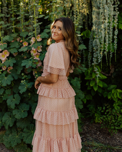 An alternate back shot of this modest dress in a blush pink color with flutter sleeves, a swiss dot fabric, and fun layered tiers.