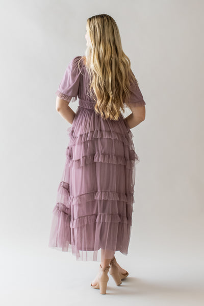 This is a blonde model wearing a dusty lavender modest dress with ruffle details and a defined waistband.