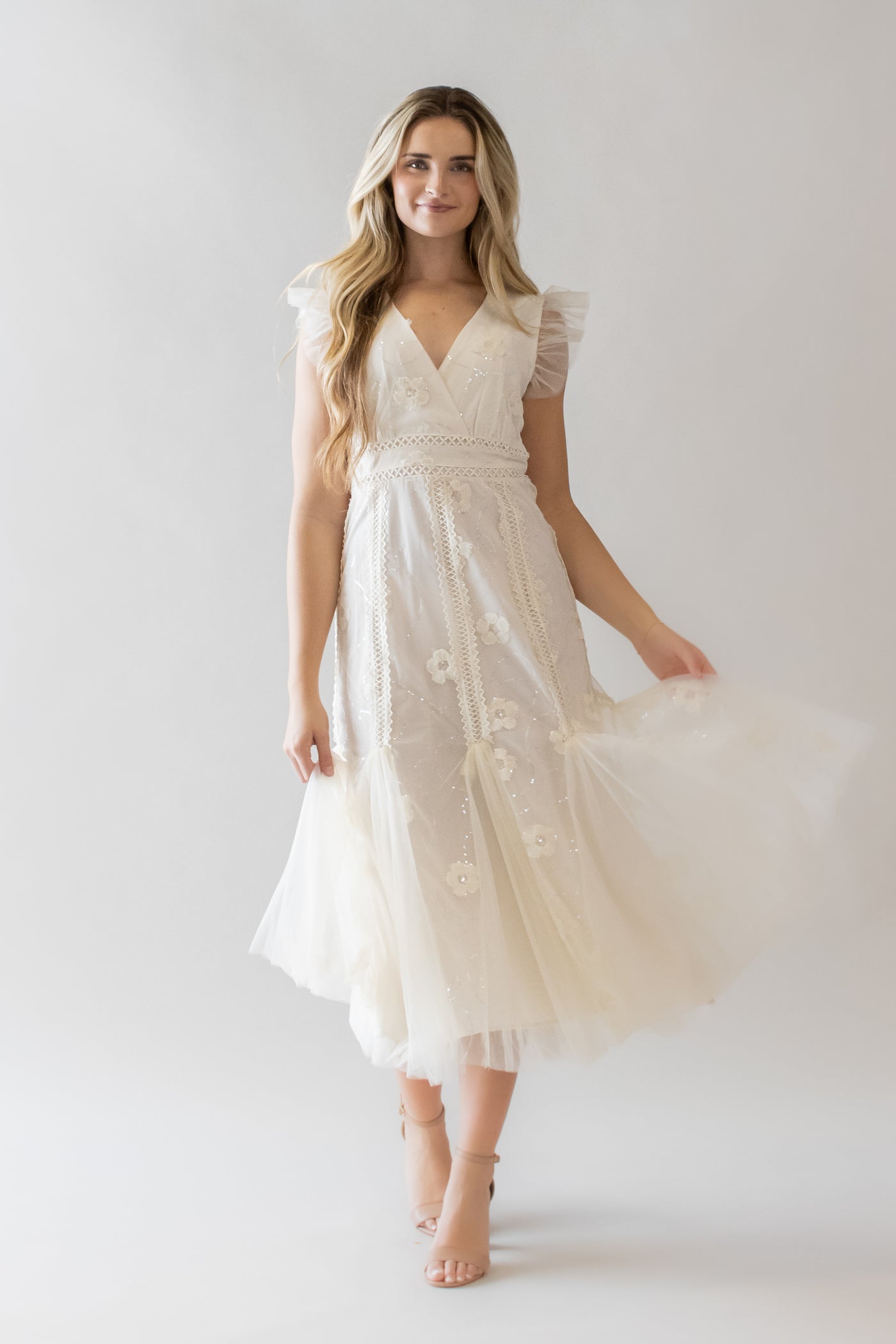This is a model wearing a white modest dress with a v-neckline and tulle details with a subtle mermaid fit.