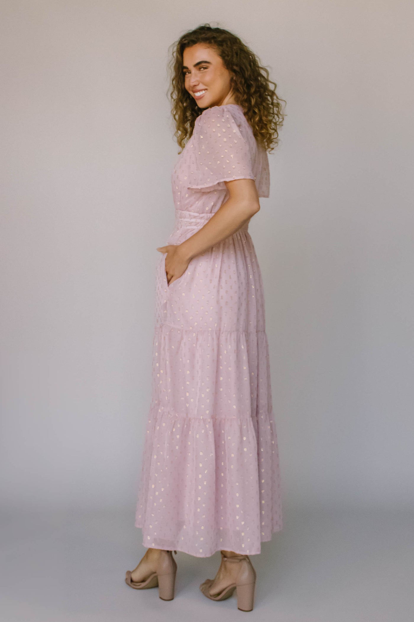 The back of a modest dress in blush pink with a gold spotted fabric, a defined waist, and flutter sleeves.