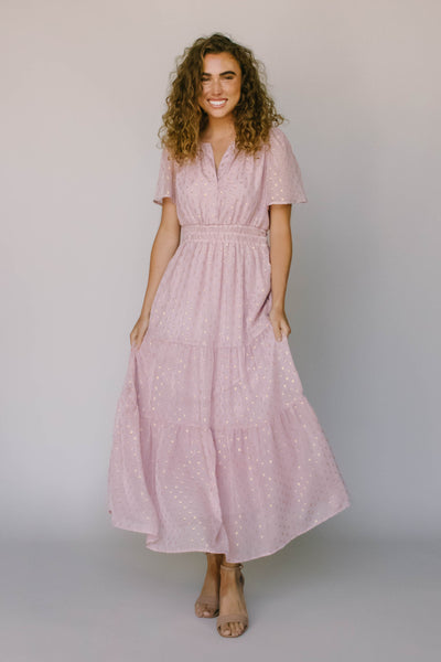 A modest dress in blush pink with a gold spotted fabric, a defined waist, and flutter sleeves.