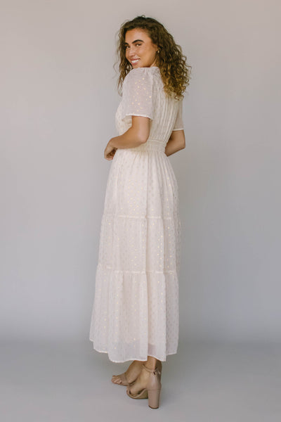 The back of a modest dress in ivory with a gold spotted fabric, a defined waist, and flutter sleeves.