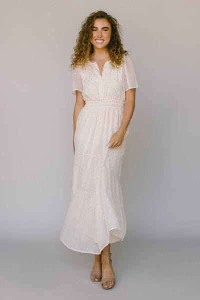 A modest dress in ivory with gold spotted fabric, slip neckline, flutter sleeves, and tiers.