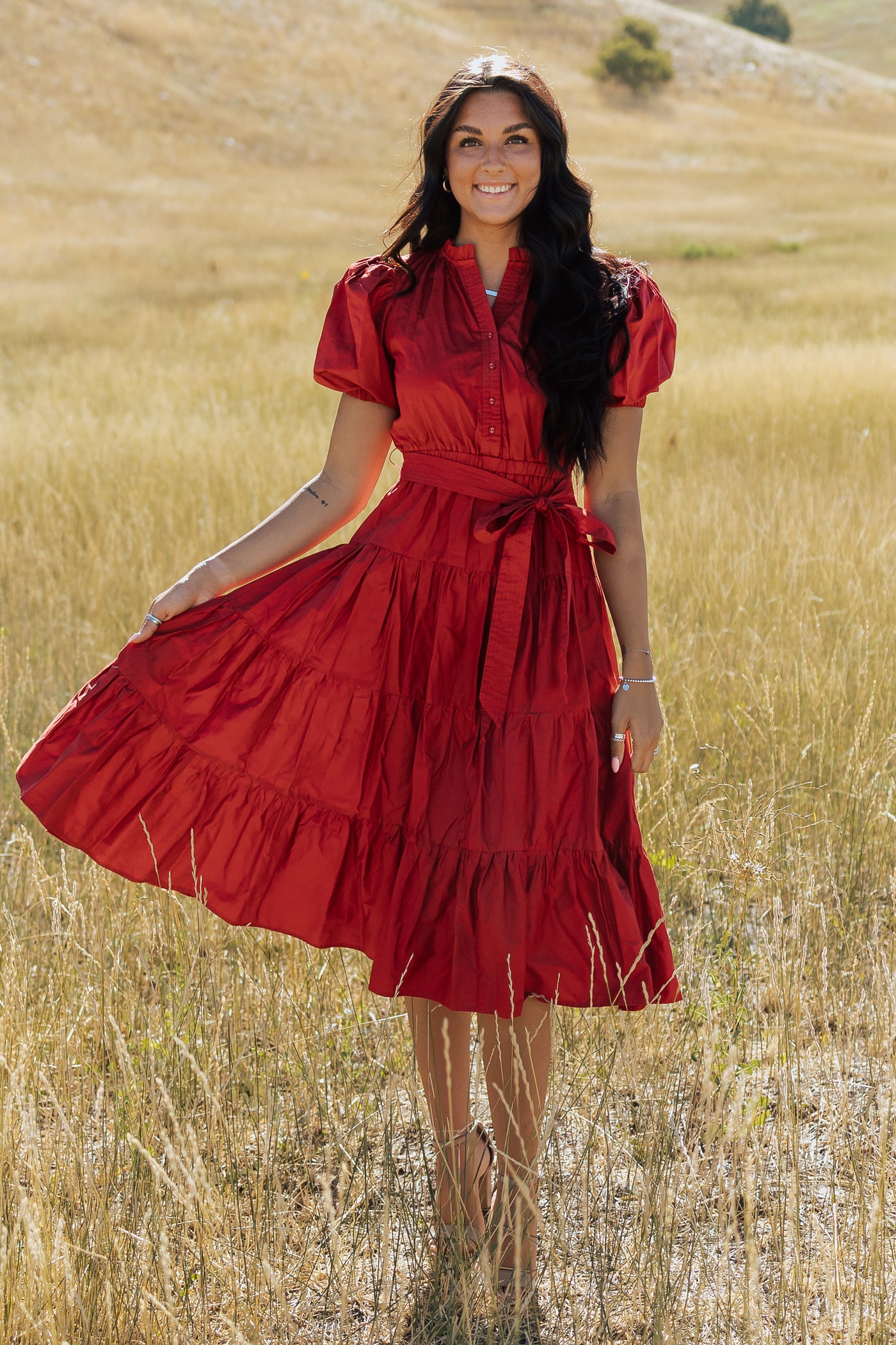 This is a front shot of a red, modest dress with a tiered ruffle skirt and a tie around the waist.