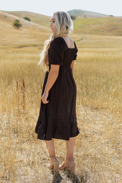 A backshot of a brown, modest dress with a square back, defined waist, and a textured fabric.