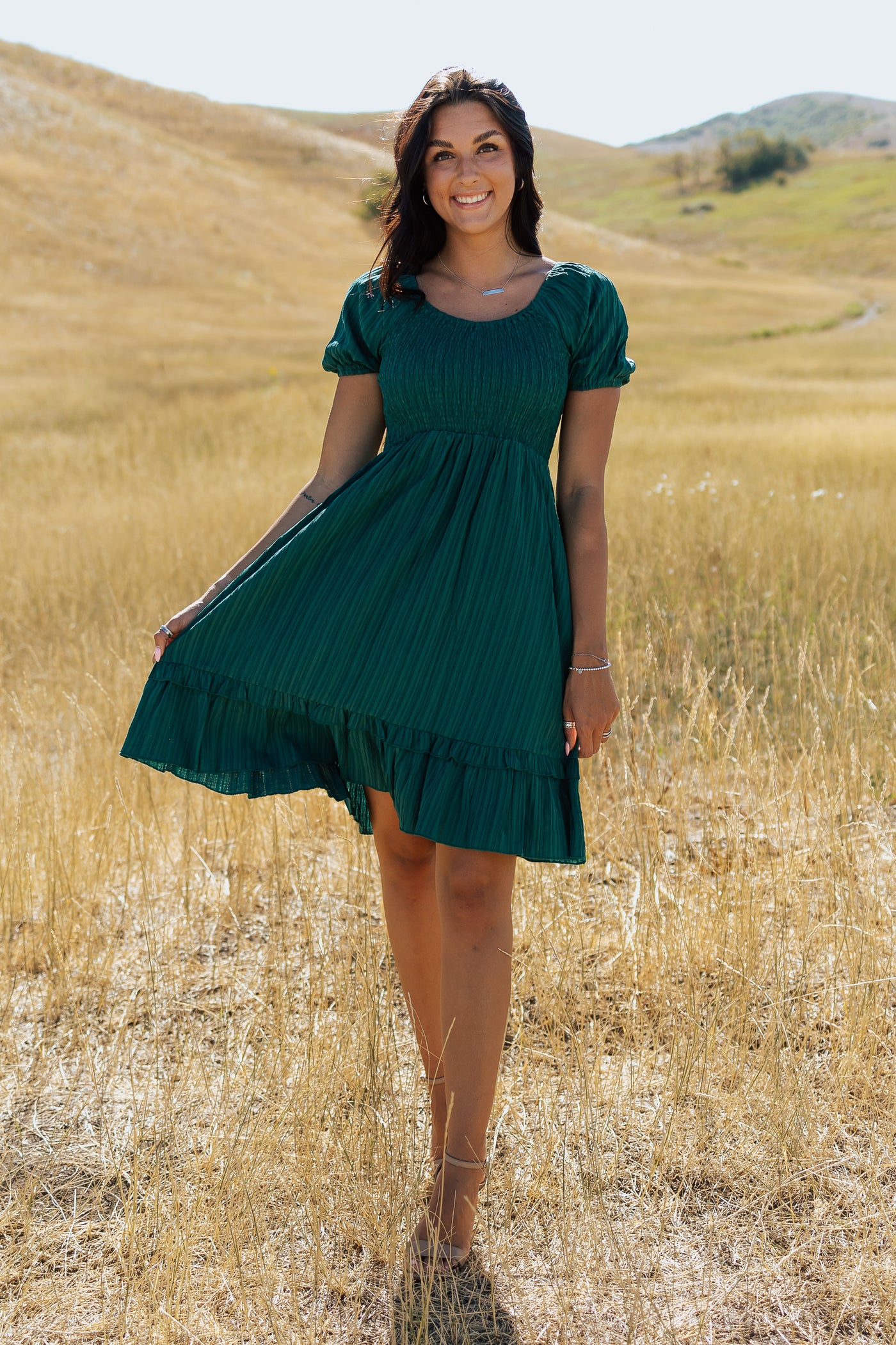 A front shot of a green, modest dress with a smocked bodice, defined waistline, and a knee-length skirt.