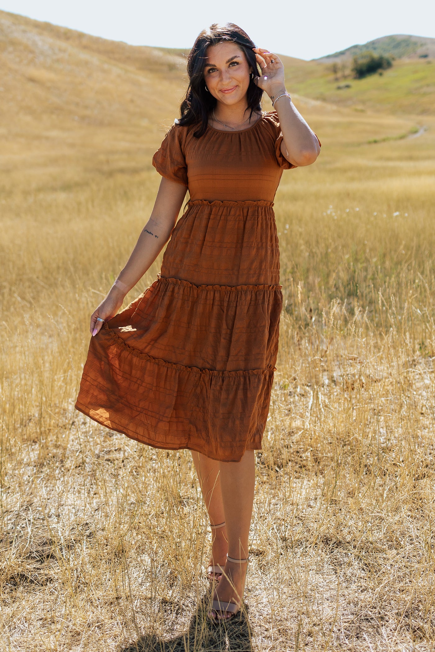 A front shot of an orange, modest dress with a scoop neckline, textured fabric and tiered skirt.