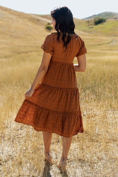 A back shot of an orange, modest dress with textured fabric and a midi length skirt.