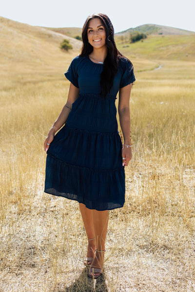 A front shot of a blue, modest dress with a textured fabric and scoop neckline.