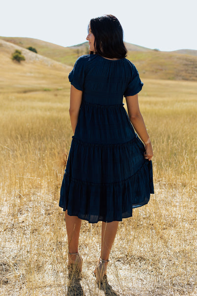 A backshot of a blue, modest dress with  tiered skirt and textured fabric.