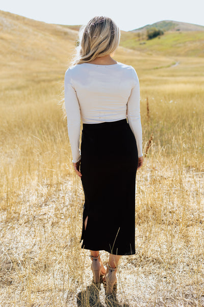 A back shot of a cream, ribbed shirt paired with a black maxi pencil skirt.