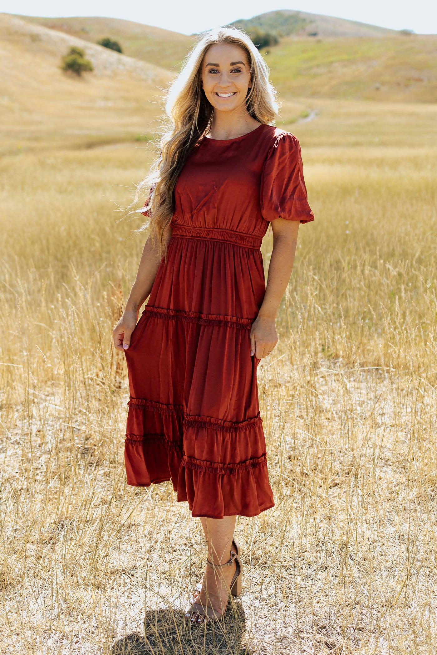 A front shot of a red, modest dress with a defined waistband, silk material, and a tiered skirt.