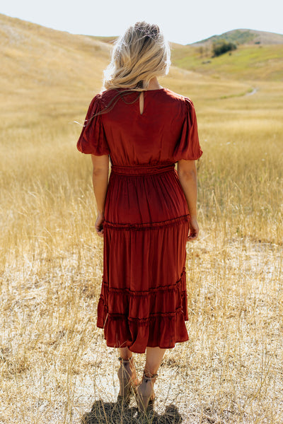 A back shot of a red, modest dress with a keyhole clasp, defined waistband, and tiered skirt.