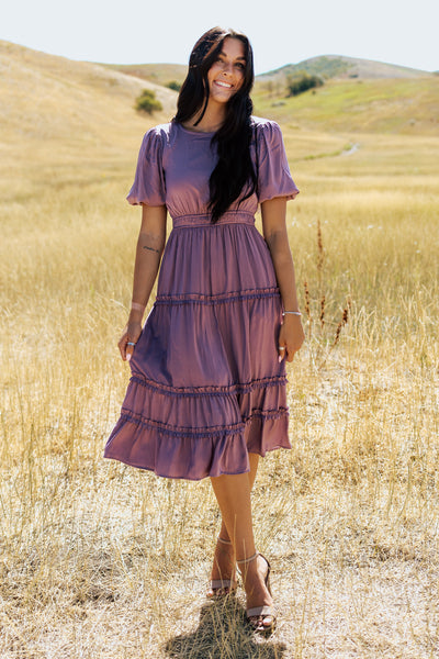 A front shot of a purple, modest dress with a defined waistband and tiered skirt.