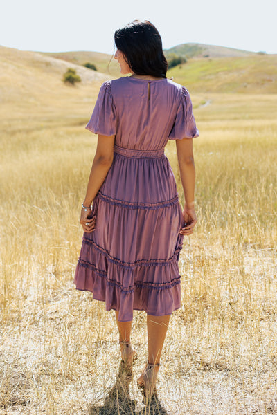 A back shot of a purple, modest dress with a defined waistband and tiered ruffled skirt. 