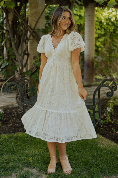 A front shot of the modest dress featuring puff sleeves, scalopped v-neck and button detailing down the front.