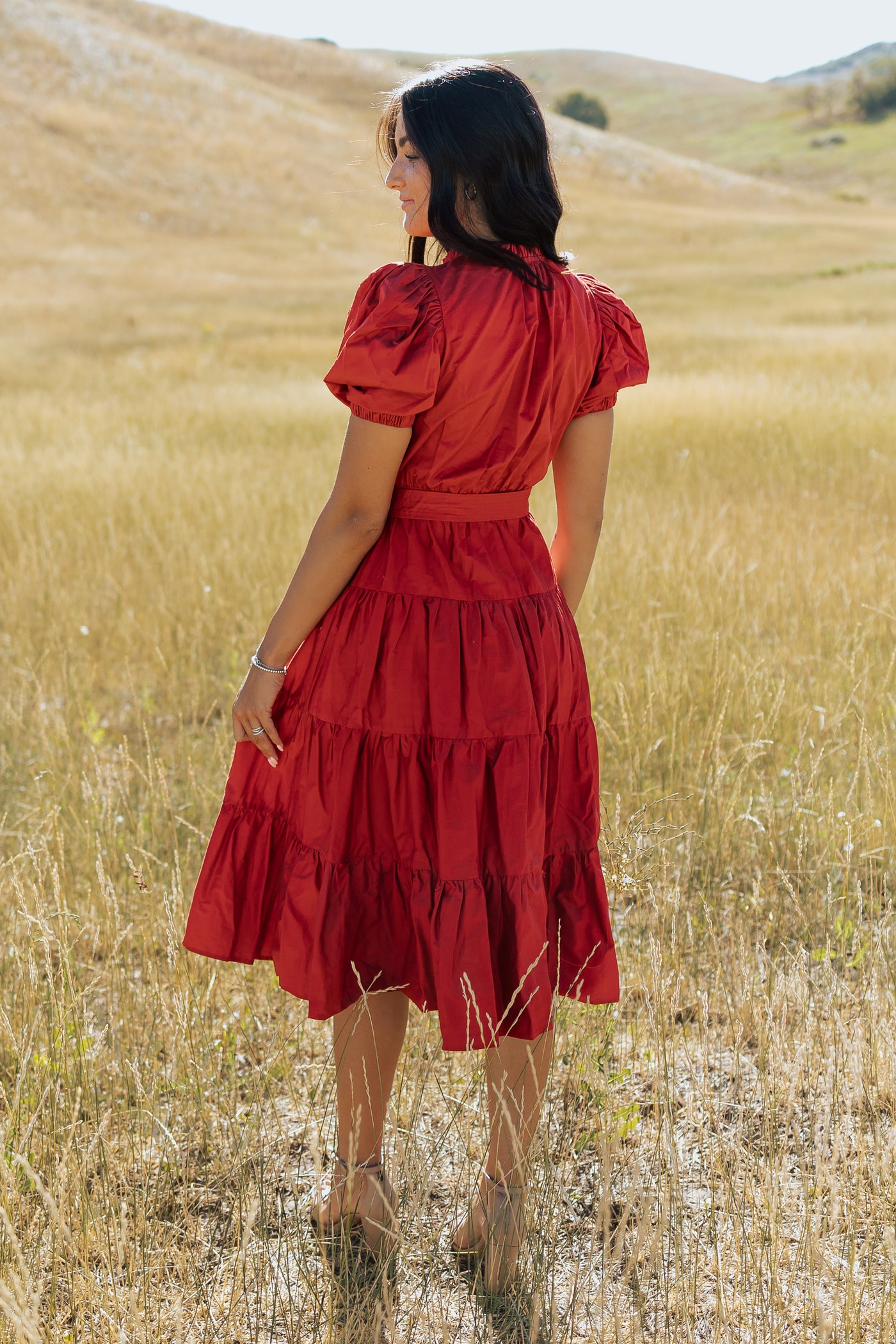 This is a back shot of a red, modest dress with puff sleeves and tiered, ruffled skirt.