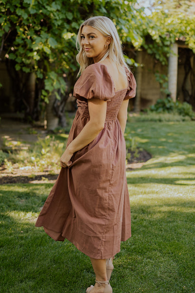 A back shot of a modest dress featuring a smocked backside, defined waistline, and puff sleeves.