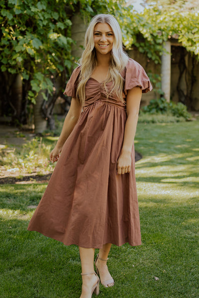 A front shot of a brown, modest dress featuring a sweetheart neckline, midi length skirt, and puff sleeves.