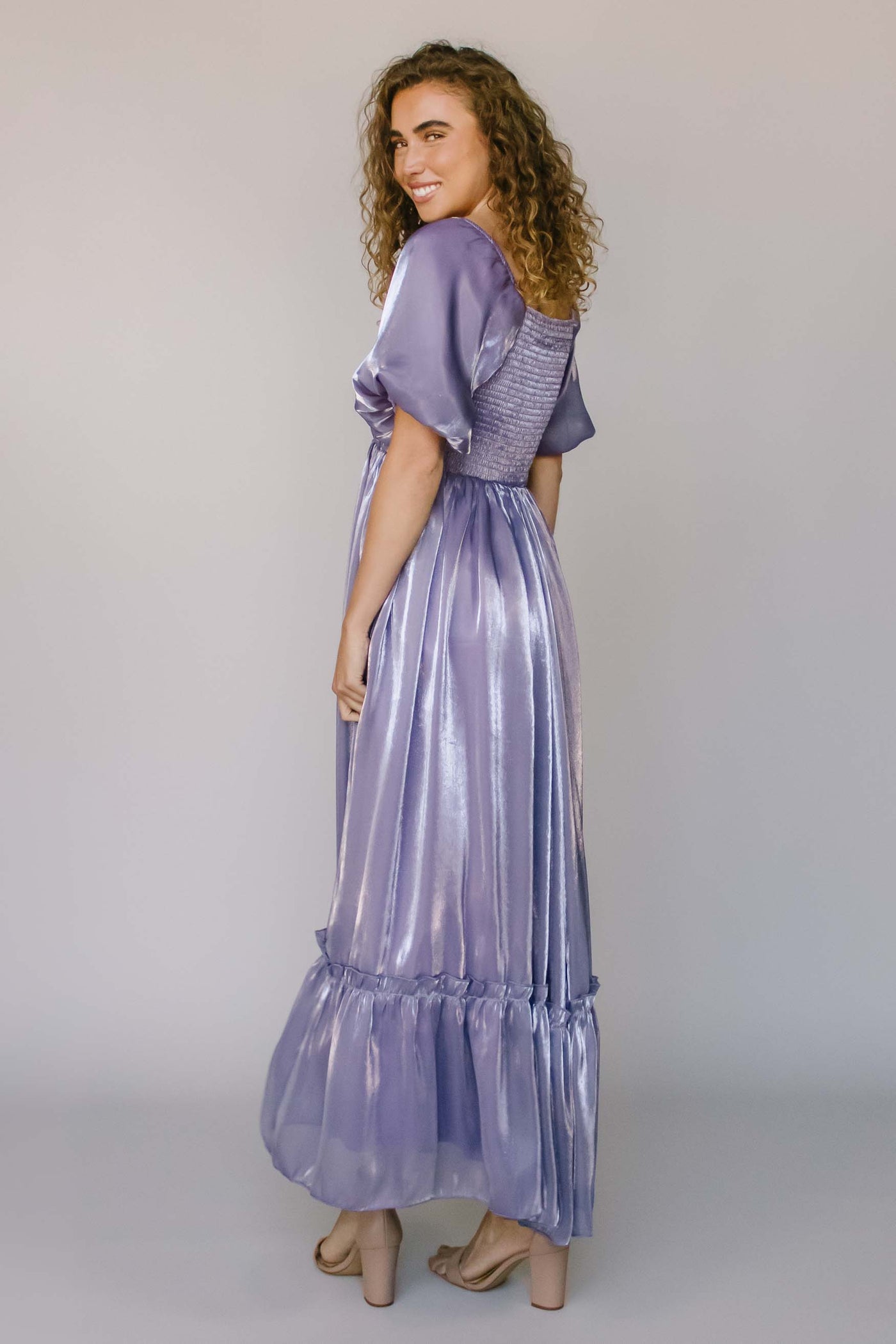 A back shot of a modest dress with puff sleeves, a square neck, and an iridescent purple fabric.
