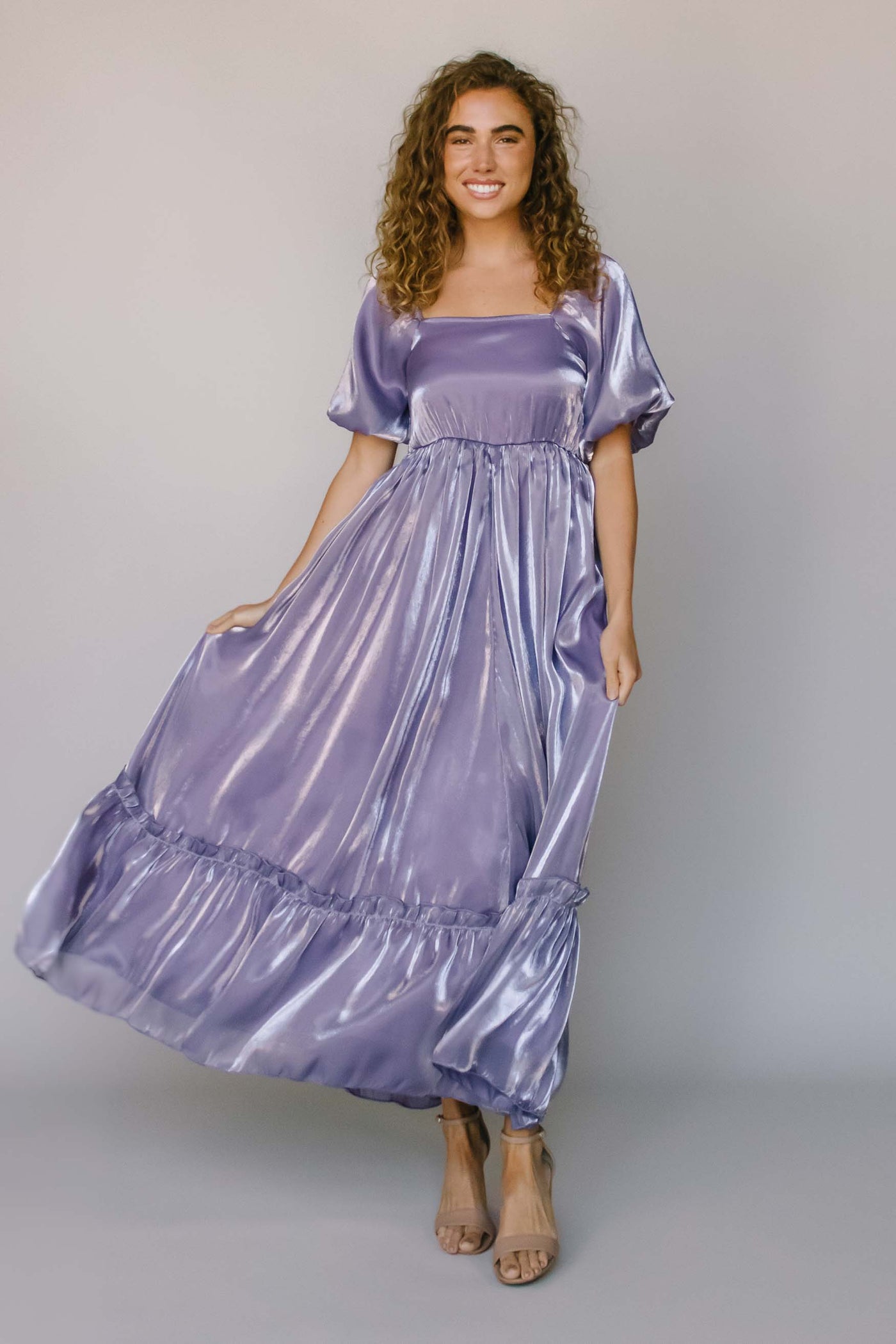 A modest dress with an iridescent, purple fabric, puff sleeves, a square neck, and a single tier.