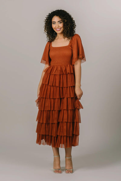This is a modest dress with tiered ruffle details and a pretty caramel/rust color.