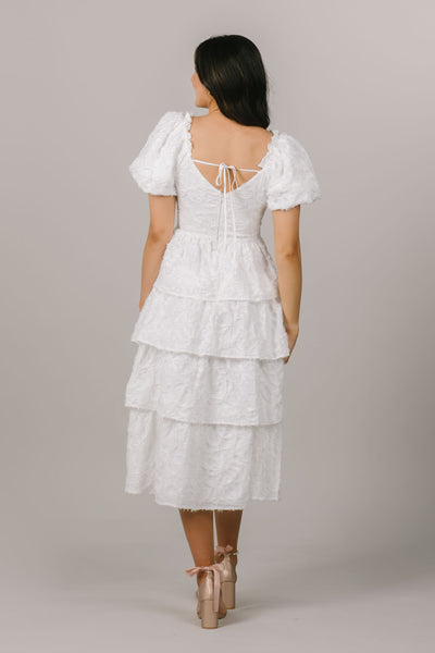 This modest dress is perfect as a white getaway dress with fun details and a tiered skirt.