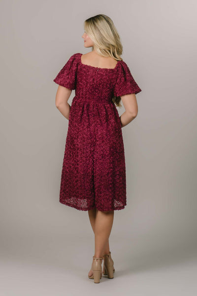 This is a back shot of a modest dress with a rose textured fabric, puff sleeve, and a gorgeous red color. 