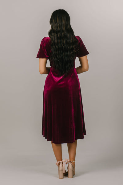 This is a modest dress featuring a crushed velvet fabric and puff sleeves as well as a v neckline.