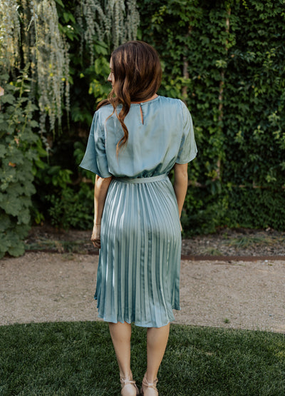A back shot of the blue, modest dress with a keyhole back, a belt to compliment the waistline, and a midi skirt.