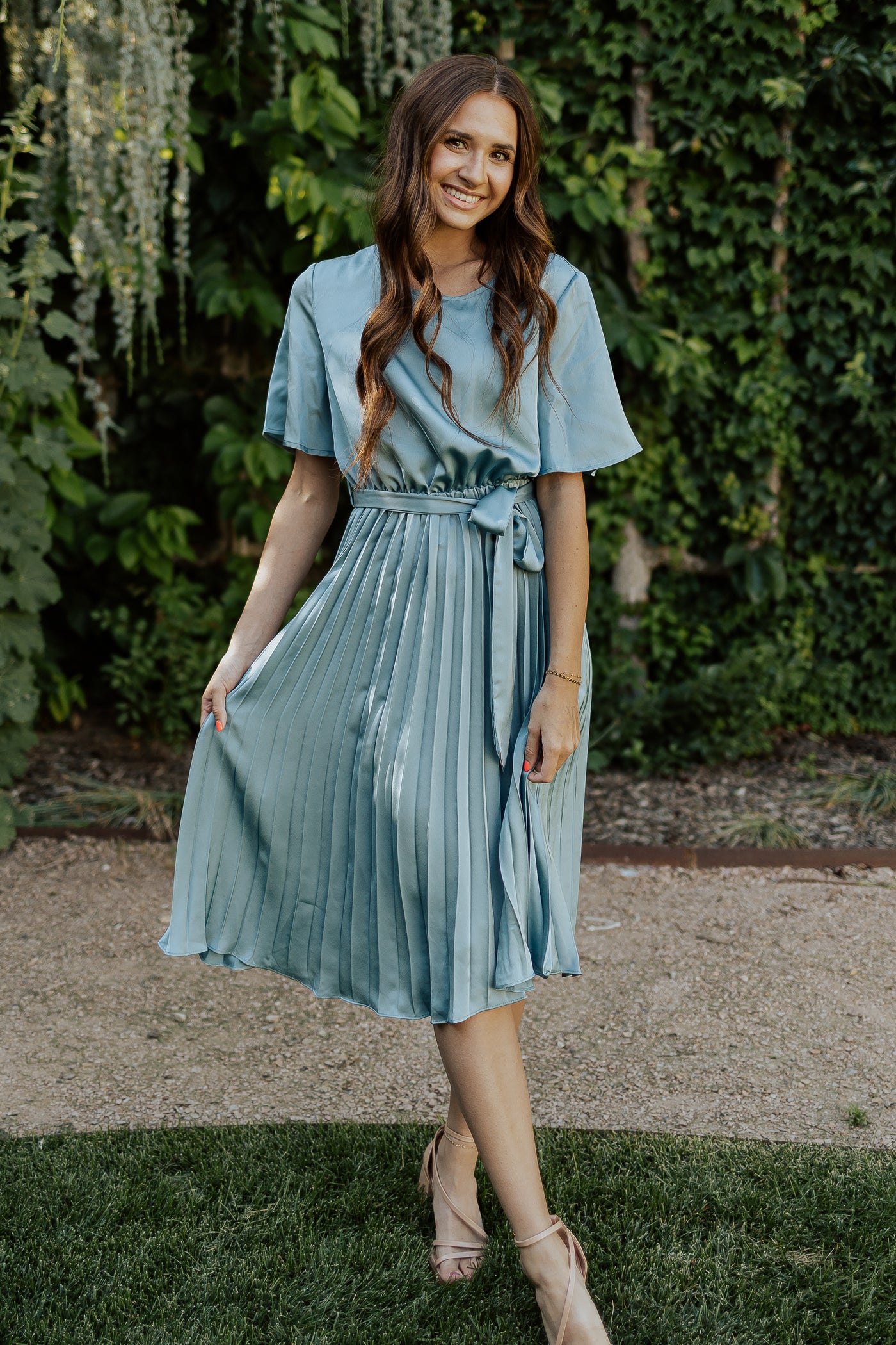 A front shot of a blue, modest dress with a high neckline, flutter sleeves, and a pleated midi skirt.