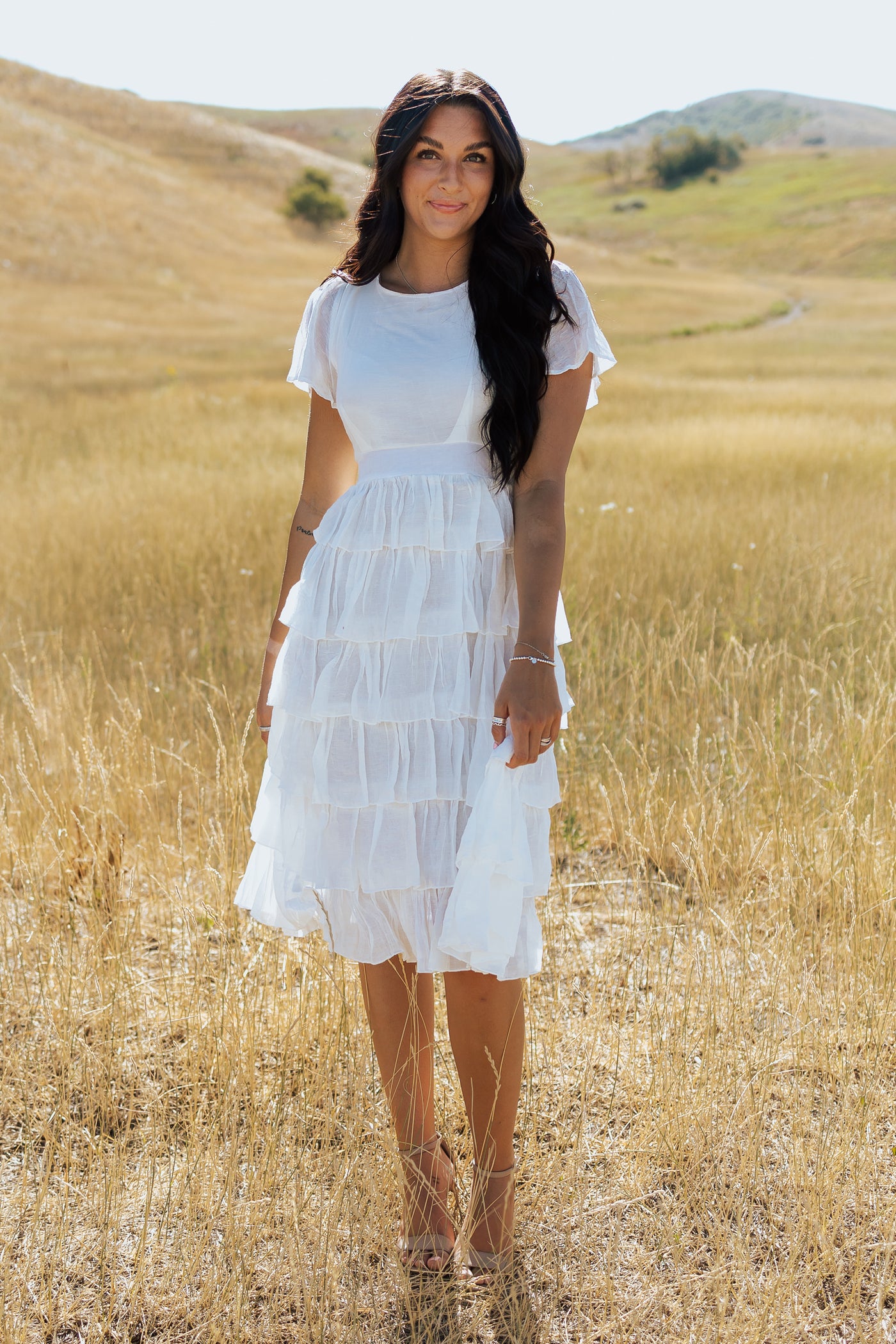 This is a front shot of  white, modest dress with tiered details and a defined waistband.