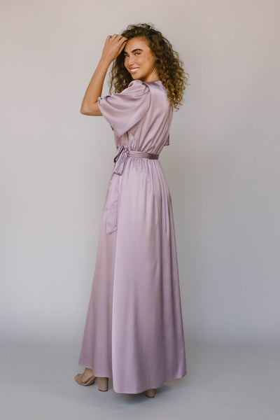 The back of a full length modest bridesmaid dress in a purple color with flutter sleeves and a tied waist.