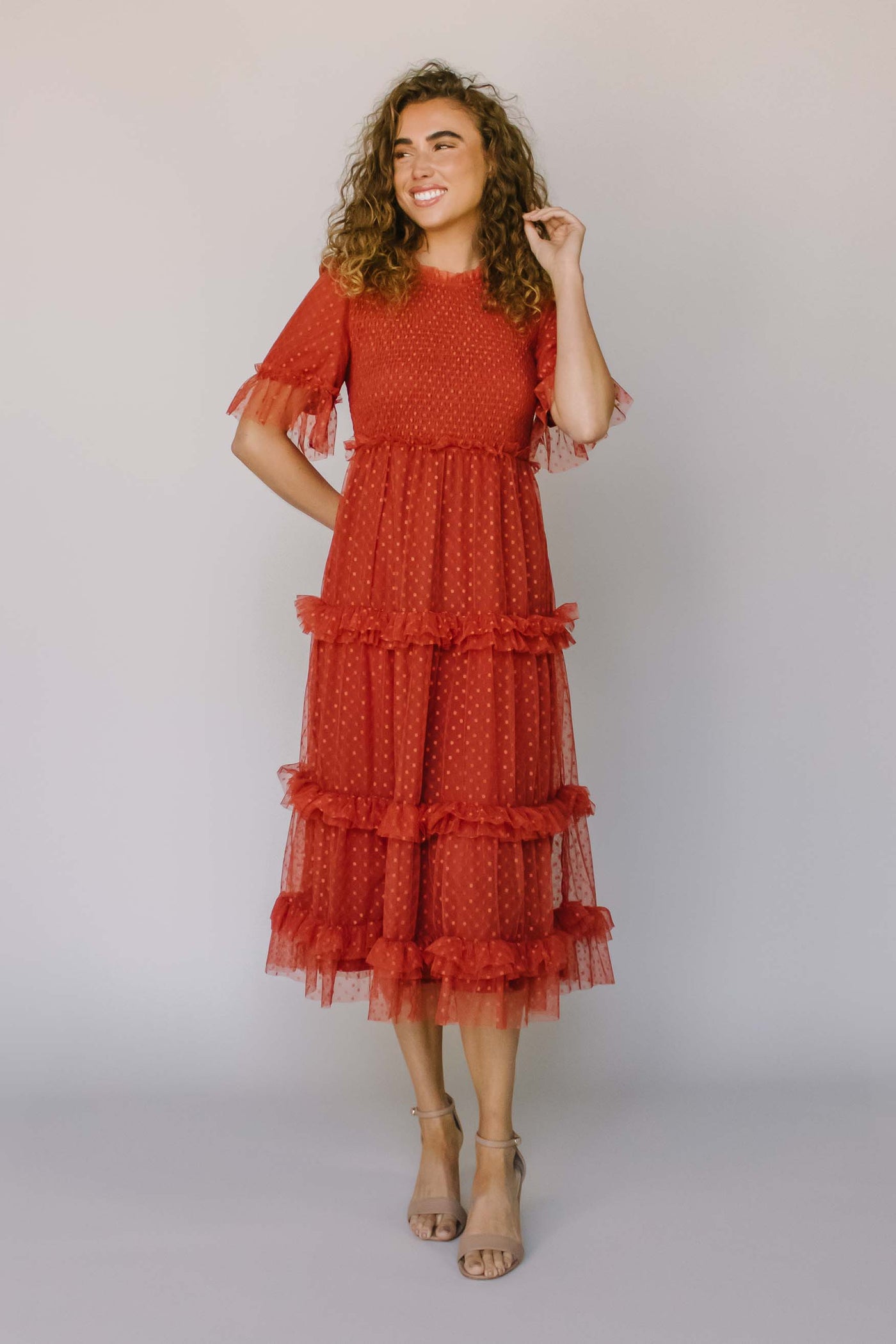 A modest dress with a rust, dotted fabric, flutter sleeves, fluffy tiers, and a smocked bodice. It also has a higher neckline.
