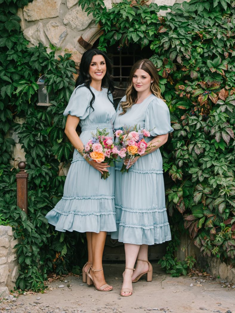 Two girls wearing matching modest bridesmaid dresses in sky blue holding flower boquets