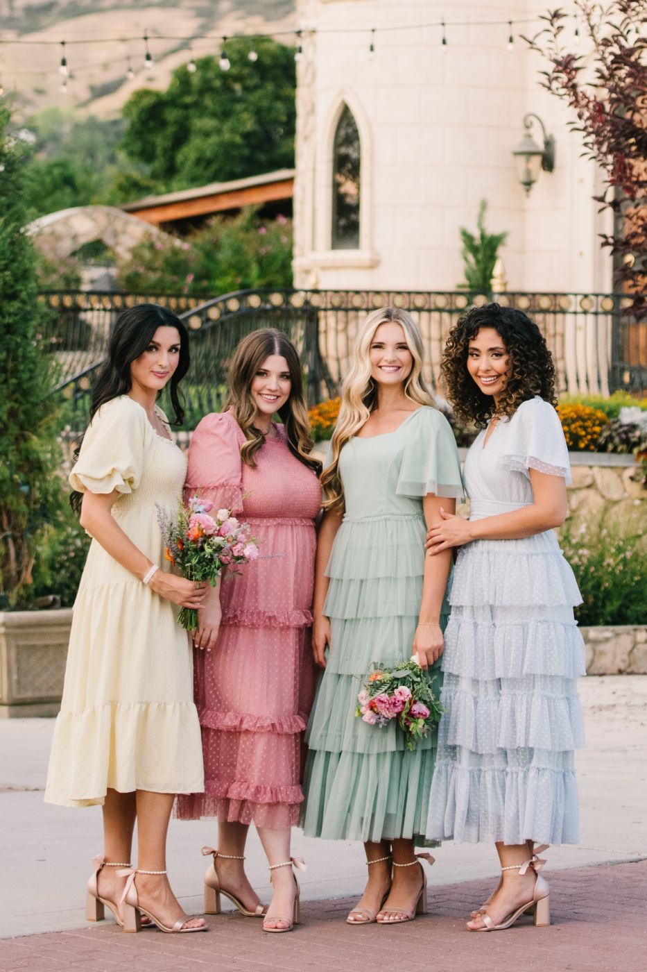 Four ladies wearing different modest bridesmaid dresses. The dresses have a soft flutter sleeve with a tiered skirt. It is the perfect modest bridesmaid dress. 