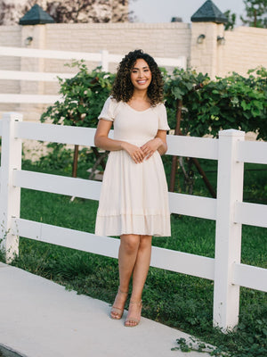 A girl standing next to a fence wearing a cream knee length modes dress