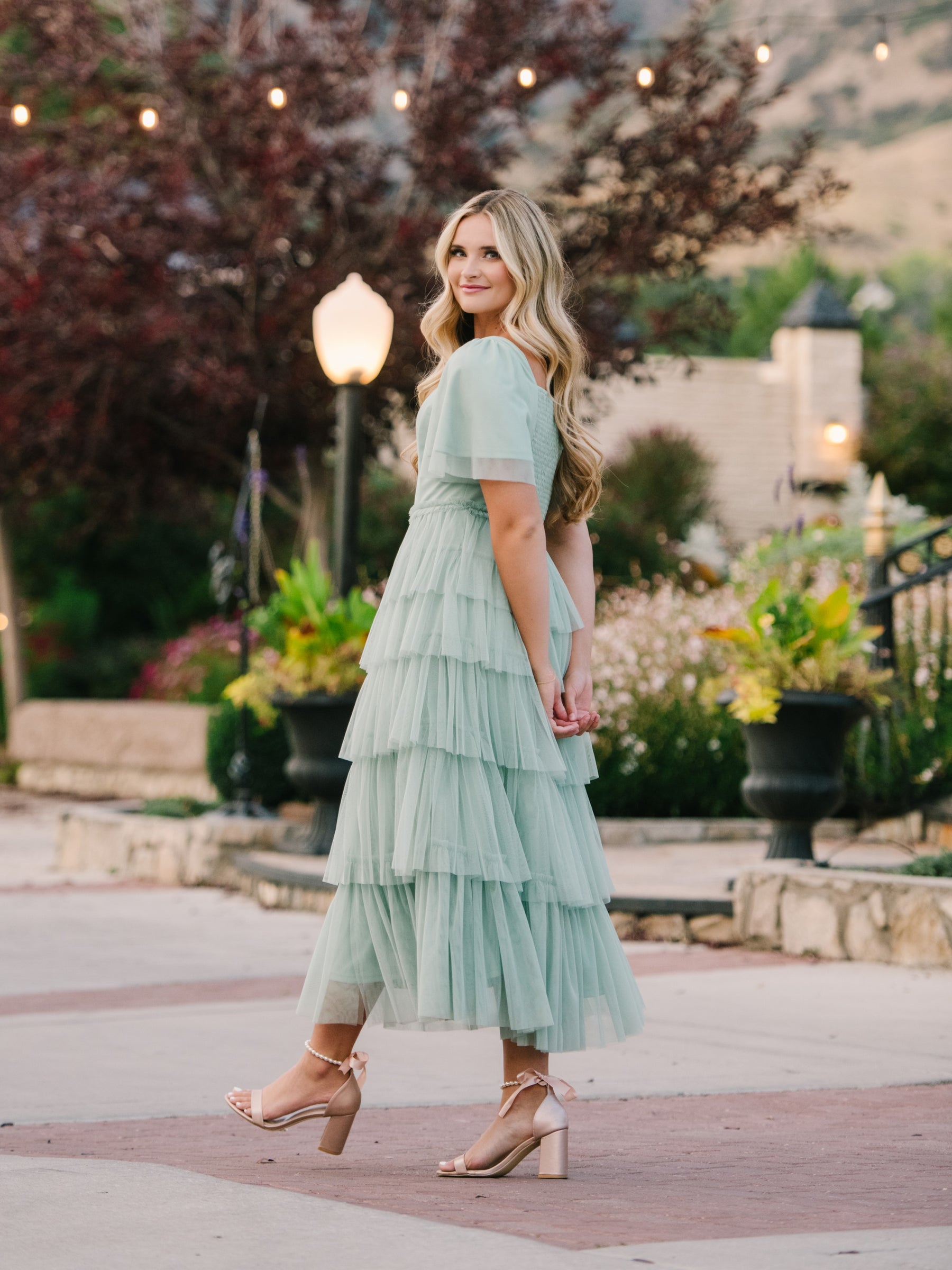 A lady walking down a pathway with a seafoam modest prom dress.