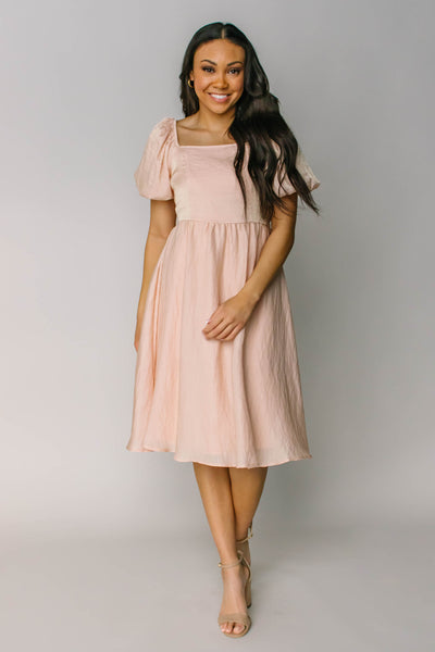 The front of a modest dress in the color blush with a square neck, puff sleeves and a stunning midi length.