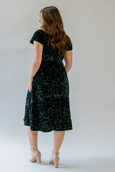 Sparkly modest bridesmaid dress with v-neckline. It is green and has sequins covering the dress. It has a higher waistline.