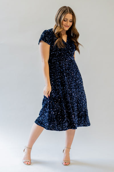 Sparkly modest bridesmaid dress with v-neckline. It is navy and has sequins covering the dress. It has a higher waistline. 