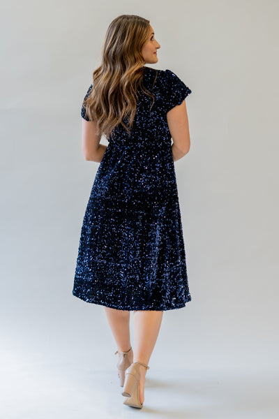 Sparkly modest bridesmaid dress with v-neckline. It is navy and has sequins covering the dress. It has a higher waistline.