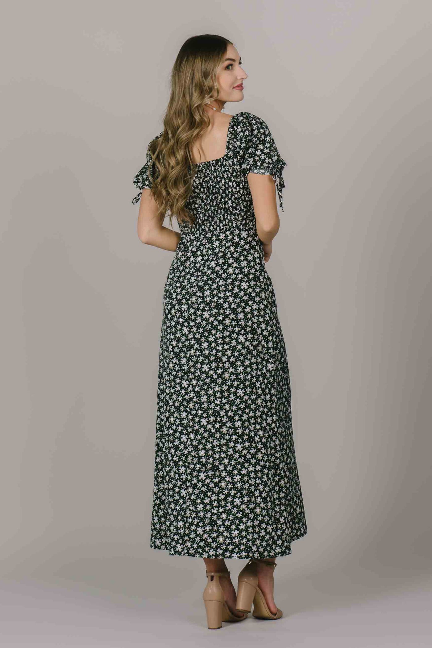 The back of a modest dress with a white floral pattern square back neckline, and puff sleeves with a bow.