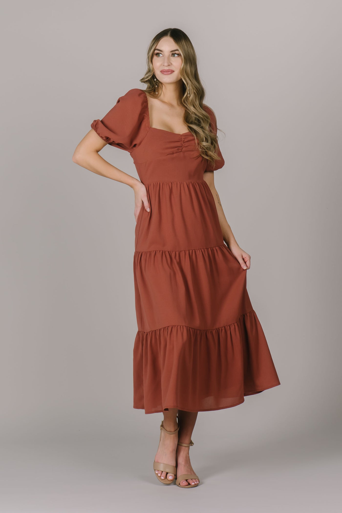 A modest dress in a beautiful rust color with a square neckline, puff sleeves, and a rouched bustline.