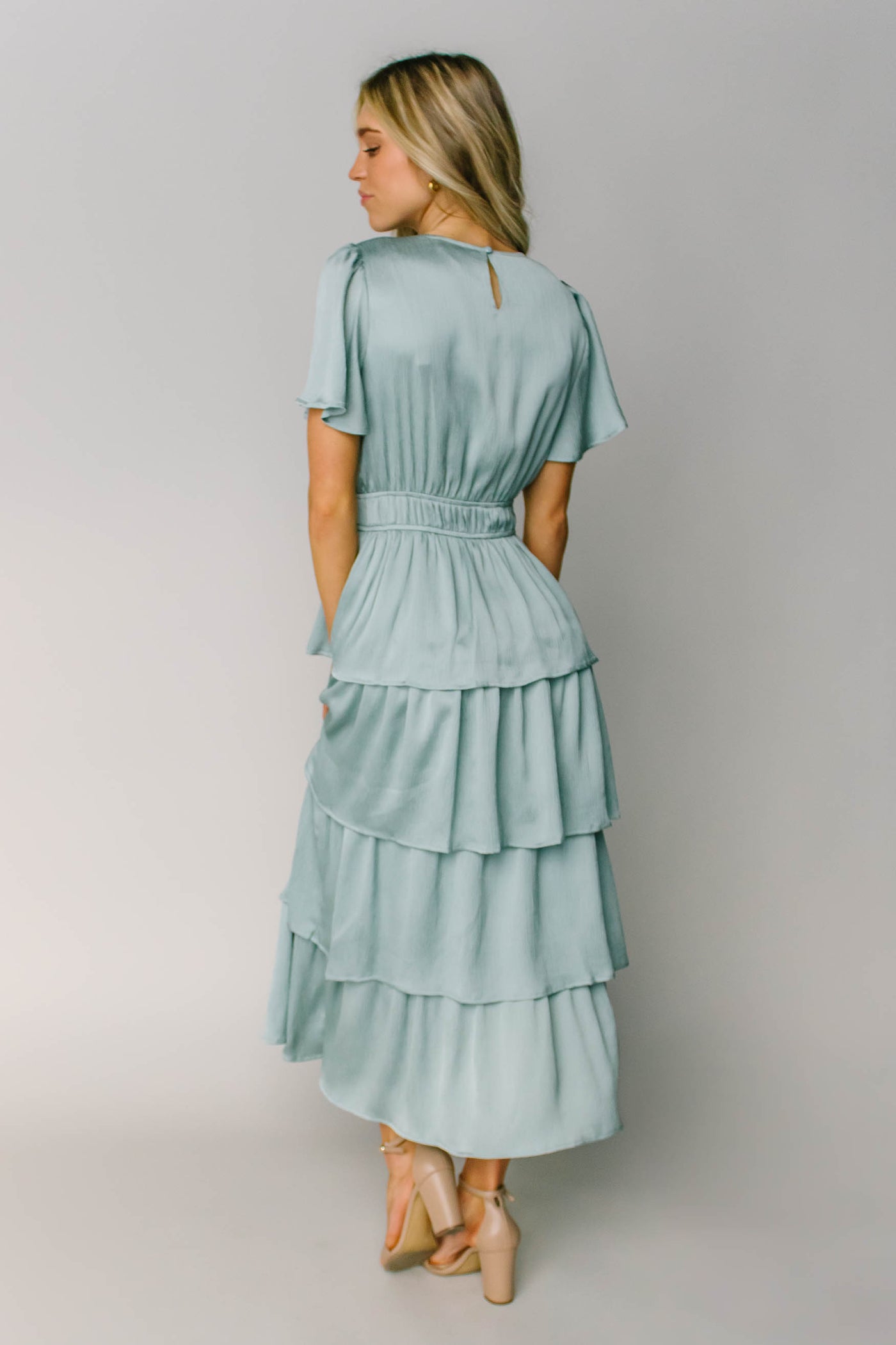 The back of a modest dress made out of a silky blue fabric, layered tiers, a keyhole, and a defined waist.
