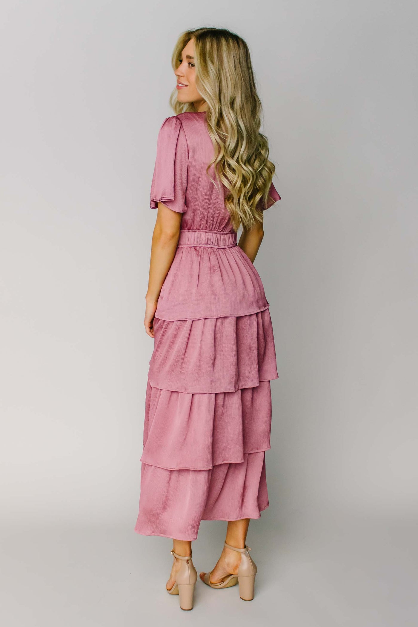The back of a modest dress made out of a silky pink fabric, layered tiers, a keyhole, and a defined waist.