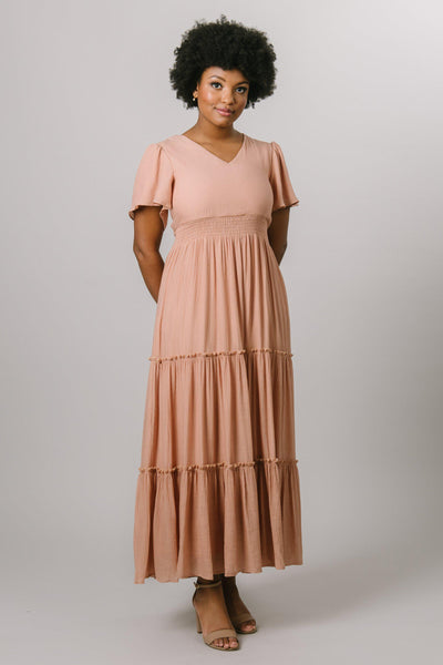 Smocked waist tiered midi dress with a v-neck and flutter sleeve in apricot. Modest Dresses - Modest Clothing - Everyday Modest Dresses - Bridesmaid Modest Dresses
